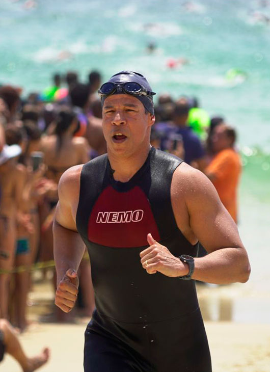 homem correndo com a roupa de neoprene da roupa e no fundo um aglomerado de pessoas